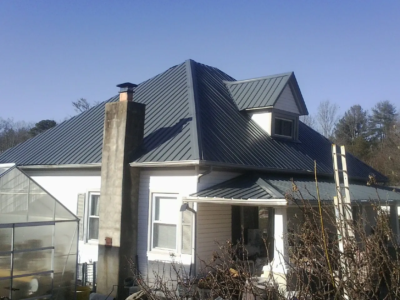 Dark blue standing seam metal roof on a white farmhouse with dormer — Slate & Tile Roof Repair by Roofing Brothers in Wynot