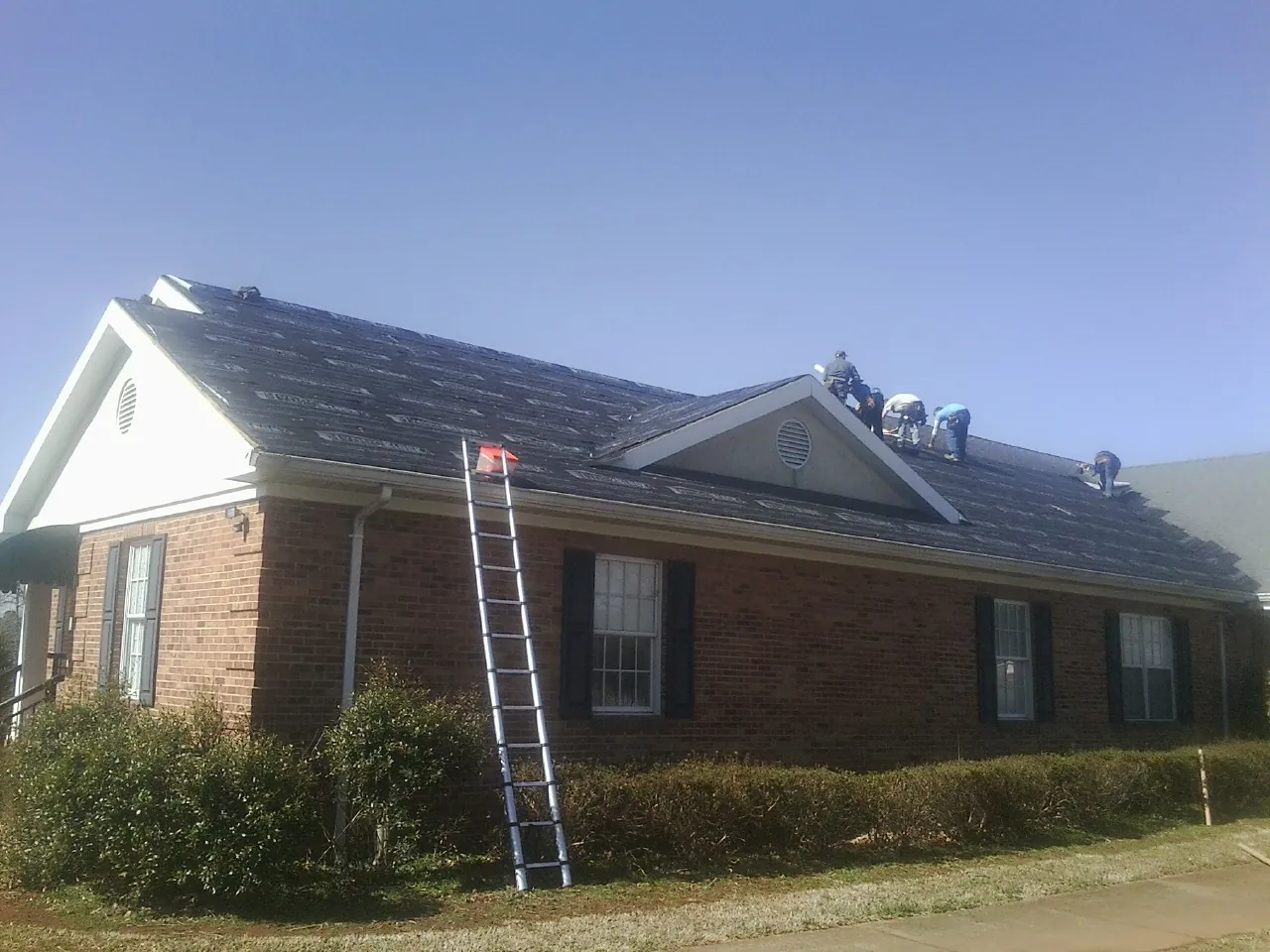 Crew tearing shingles off a brick ranch roof with a ladder set — Metal Roof Repair work by our crew in Wynot