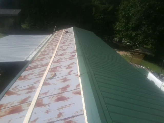 Old rusted panels beside newly installed green metal roofing — Wind Damage Roof Repair by Roofing Brothers in Wynot