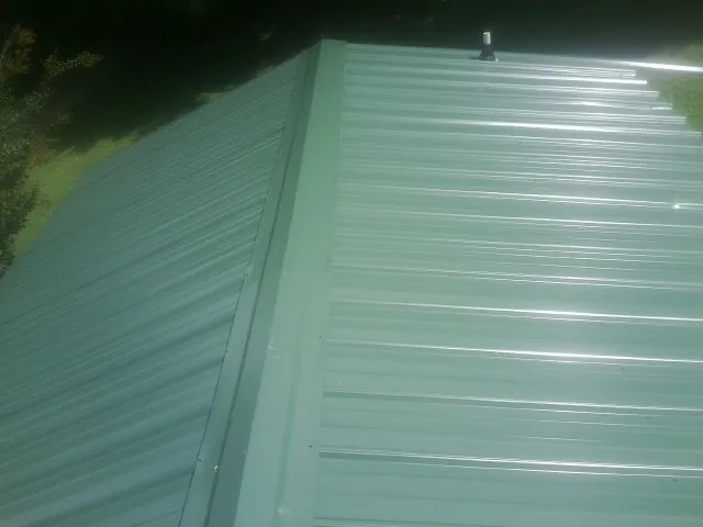 New green metal panels meeting at the ridge of a roof — Flat Roof Repair work by our crew in Wynot