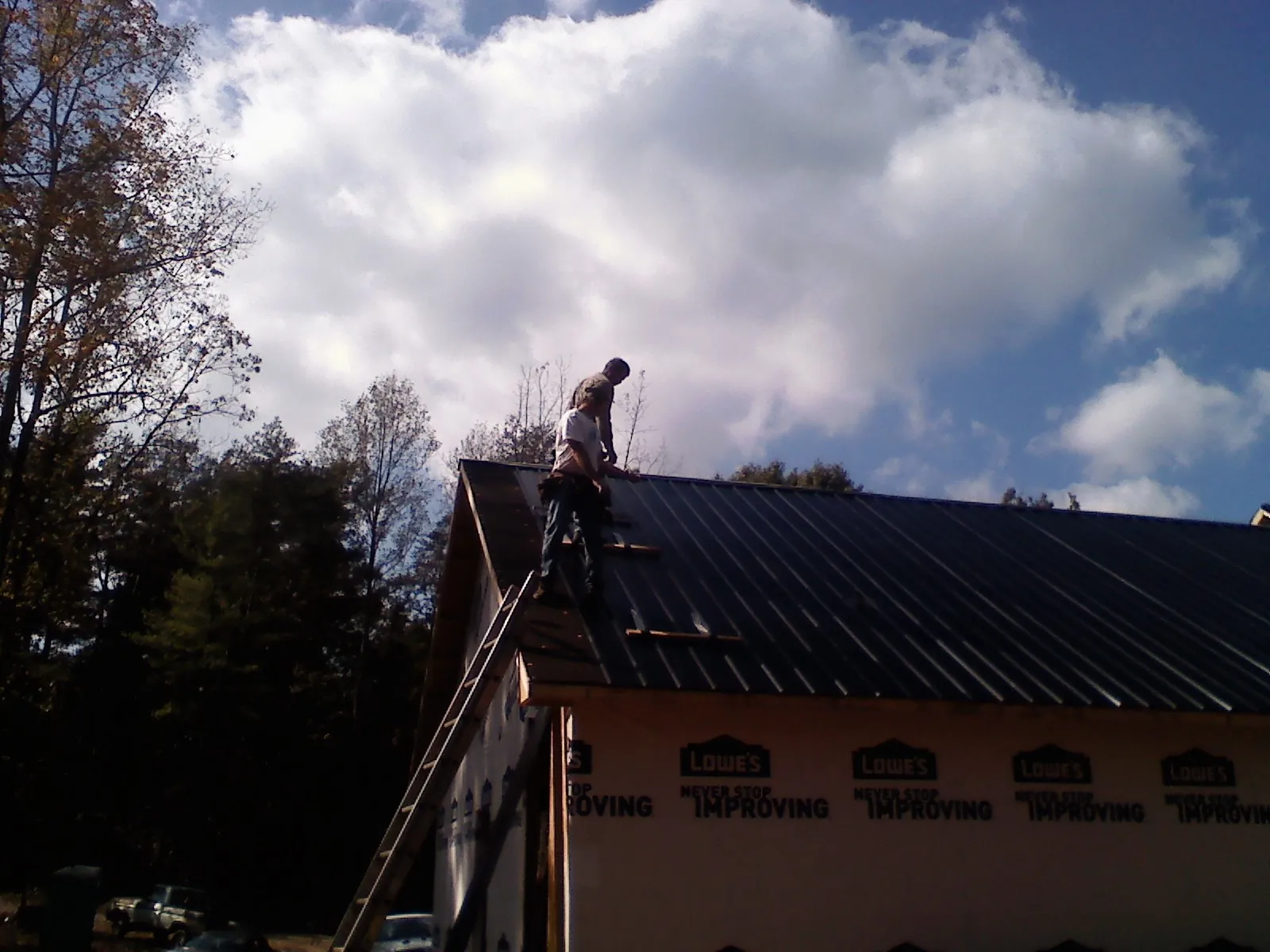 Roofer fastening dark metal panels high against a cloudy sky, from a Roof Inspection job in Wynot
