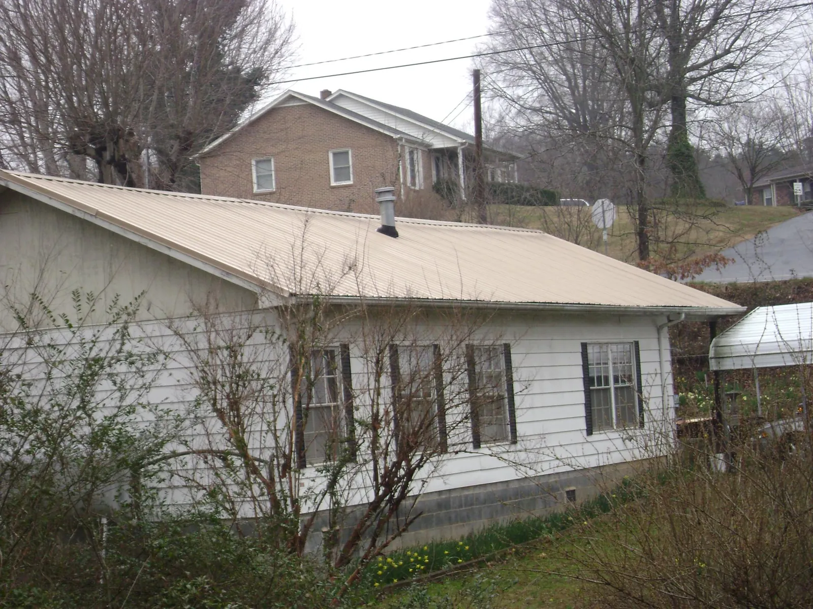 Tan metal roof on a white sided house set into a hillside — Commercial Roofing by Roofing Brothers in Wynot