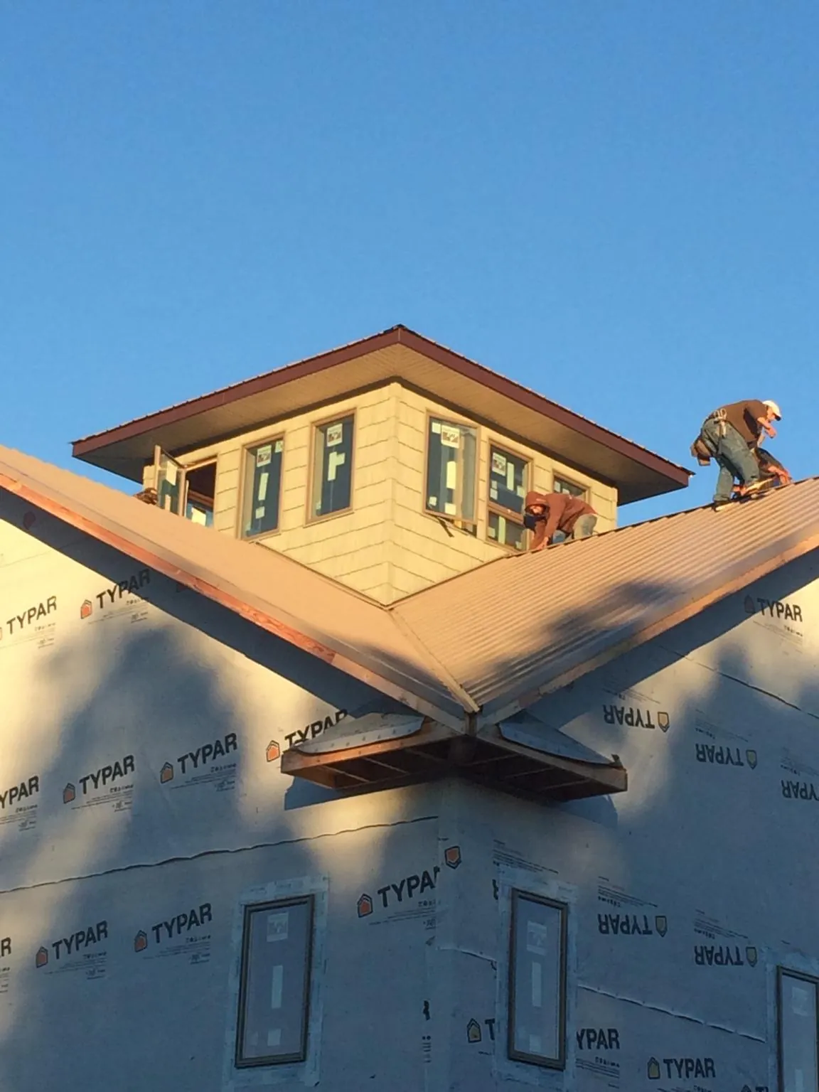 Roofers working around a rooftop cupola on a new metal roof at sunset — Roof Waterproofing in Wynot by Roofing Brothers